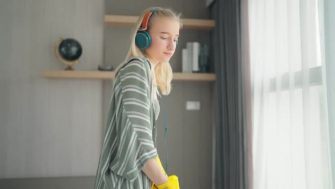年轻女子金发清洁地板在家通过耳机享受音乐