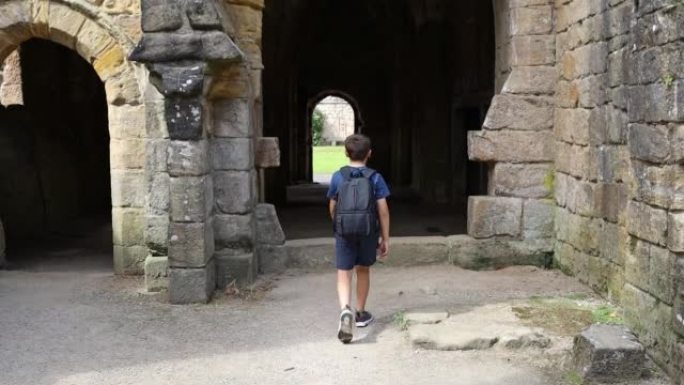 小男孩走过喷泉修道院的中世纪拱门