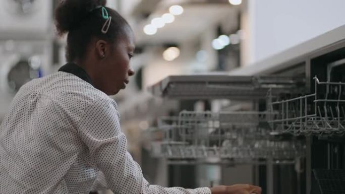 年轻的黑人妇女正在为公寓的新厨房选择洗碗机，在家用电器商店购物