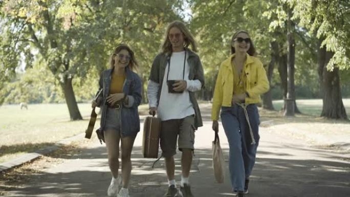 无忧无虑的20世纪60年代嬉皮士沿着阳光明媚的夏日道路行走并交谈。积极的高加索男女在户外旅行。反文化