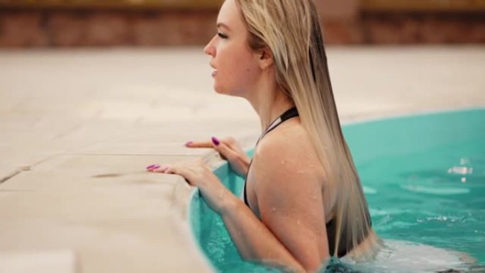 美丽的金发女人在现代水疗酒店的露天游泳池游泳，享受热水浴