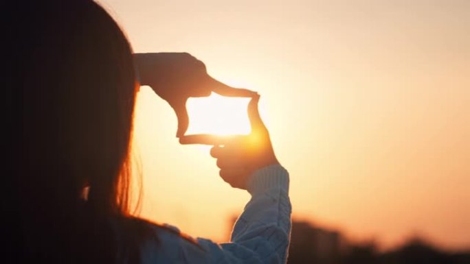 新年计划和视觉概念，女人的手与日落做框架手势，女性捕捉日出。