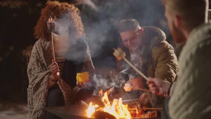 成年黑人妇女在冬夜圣诞节在朋友圈篝火中烤棉花糖
