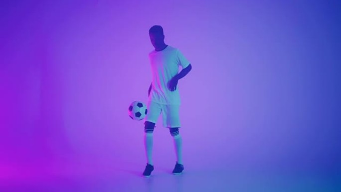 黑人一名球员在黑暗的工作室里玩足球，地板上有霓虹灯，慢动作中有红色和蓝色的灯光效果。非洲职业足球运动