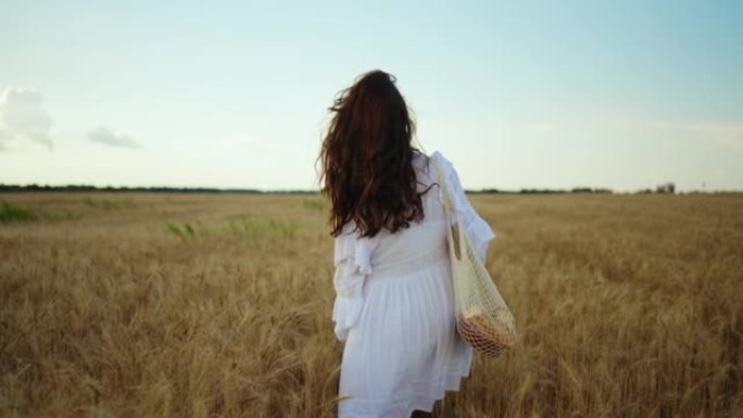 穿着白色连衣裙的美丽黑发女人走在金色的麦田上，举起双手享受美丽