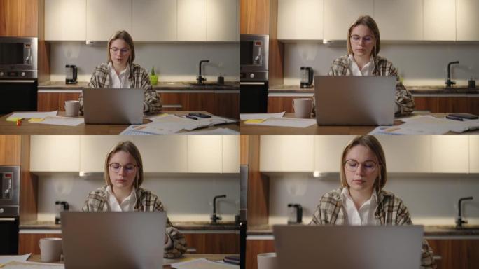 变焦相机一个戴眼镜的女人坐在桌子旁，坐在笔记本电脑和毡尖笔在图表上标记数据的远程工作。远程学习学生在