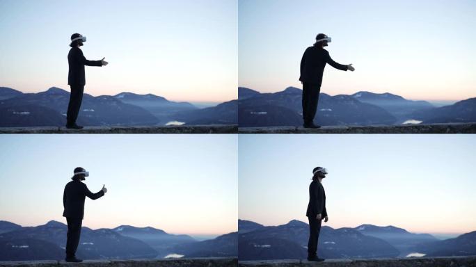 男子戴着VR虚拟现实护目镜在户外山中俯瞰日落灯光下的湖，与想象中的人握手