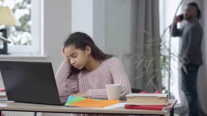 疲倦的青少年学生睡着了，正在听笔记本电脑上的在线课程，因为男人在智能手机上的后台行走。检疫上疲惫不堪