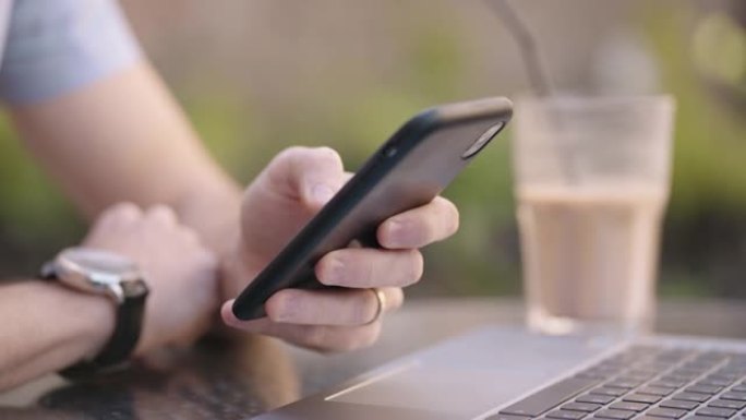 特写一名拿着手机的男子正在从事网上银行，在互联网上购买并在社交网络上写信息，同时坐着笔记本电脑