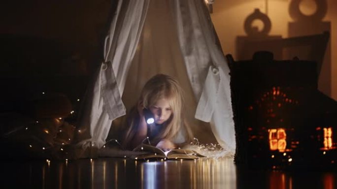 帐篷下用手电筒看书的女孩。孩子在带灯笼的帐篷里做梦。