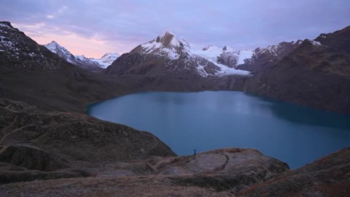 女越野跑运动员在日出时沿着山路奔跑，可以看到雪峰和后面的高山湖泊
