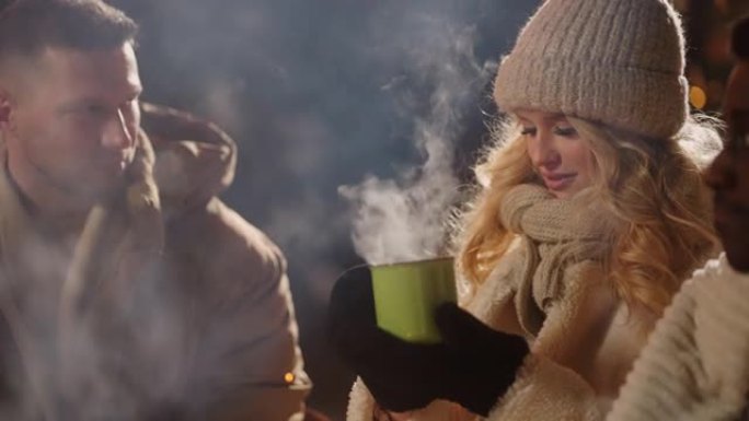 冬夜，快乐的女人和她的朋友在户外用金属杯喝热酒或茶