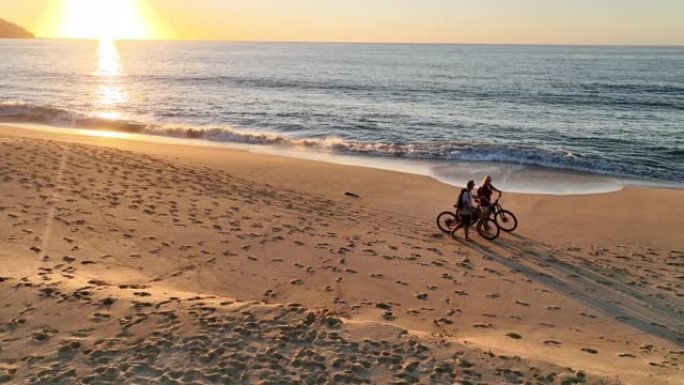 夫妇在空旷的海滩上推自行车的鸟瞰图