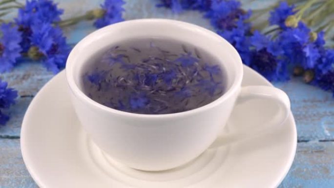 复古浅蓝色木制桌面上有白色和蓝色的花。用白色杯中的花花酿造tisanes。