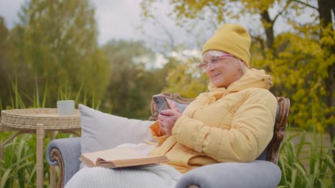 患病的老年妇女患者在外面的椅子上使用手机