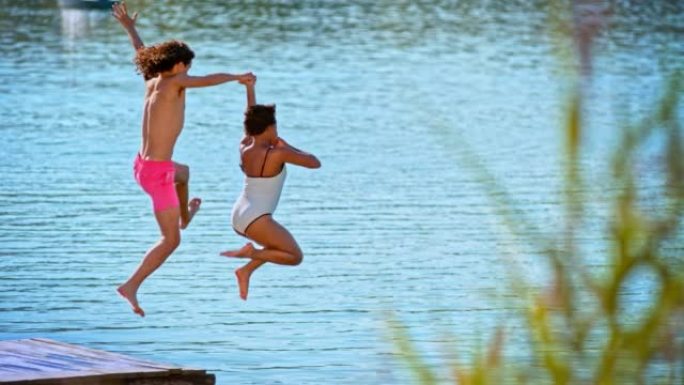 SLO MO LD年轻夫妇在阳光下从码头跳入湖中