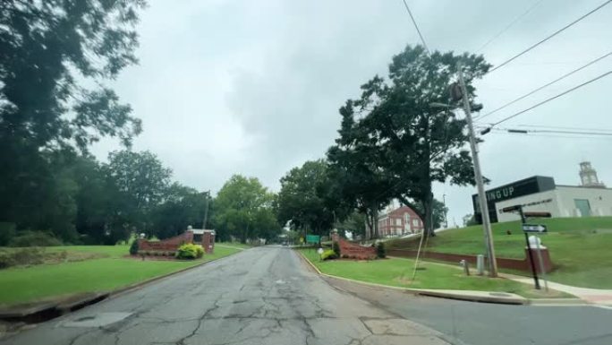 在一个风雨如磐的灰色日子里，路过企业并开车进入阿拉巴马州塔拉迪加的塔拉迪加学院入口的汽车视点镜头