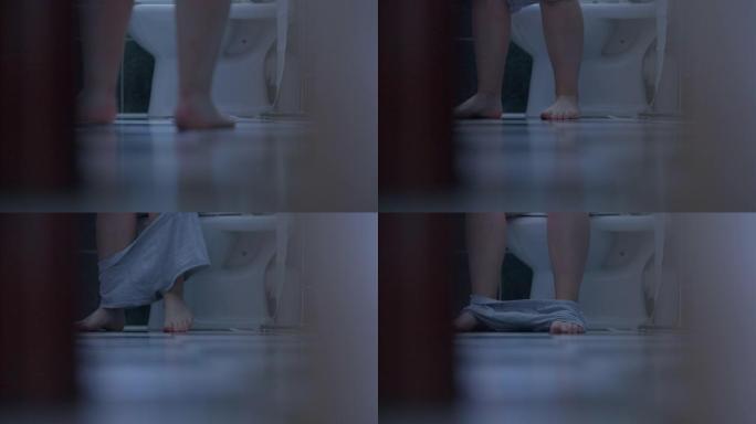 赤脚的白人男性双腿进入厕所，坐下来脱下内裤，轻拍脚。无法辨认的男人早上在家使用浴室。常规和卫生概念。