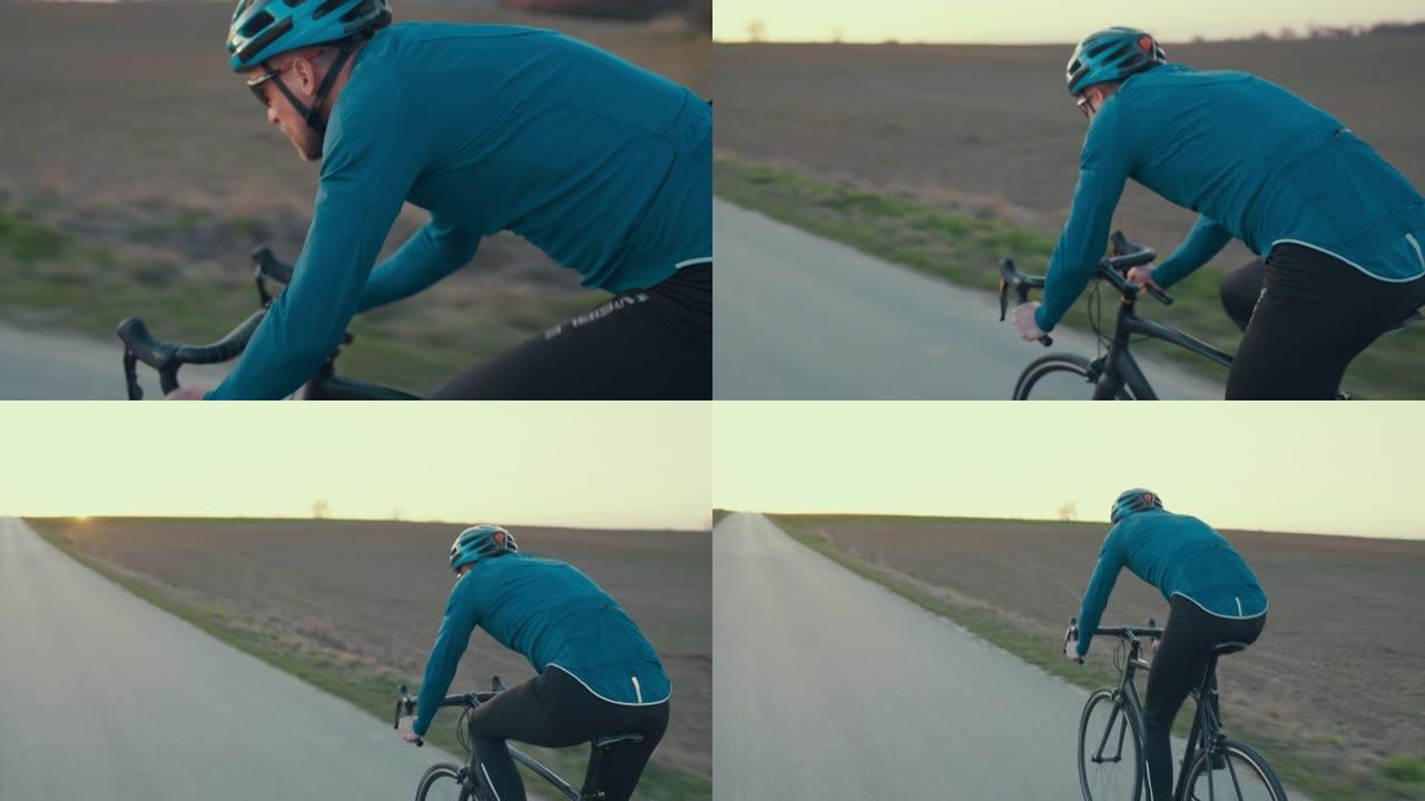 男性公路自行车手在空旷的地方超速行驶的后视图。春天的日落