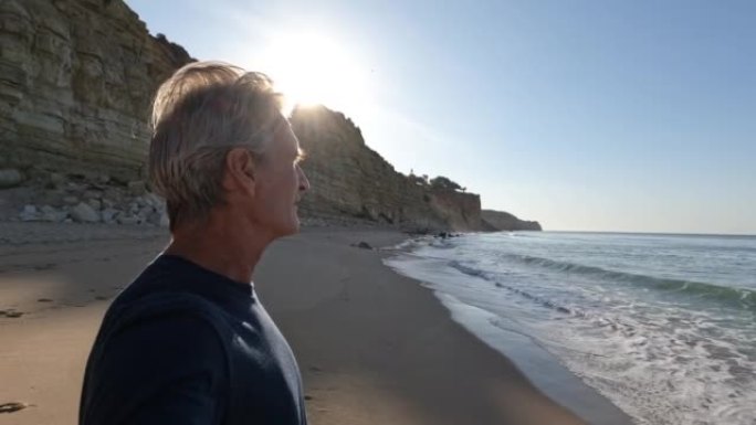 成熟的男人在日出时沿着空旷的海滩散步
