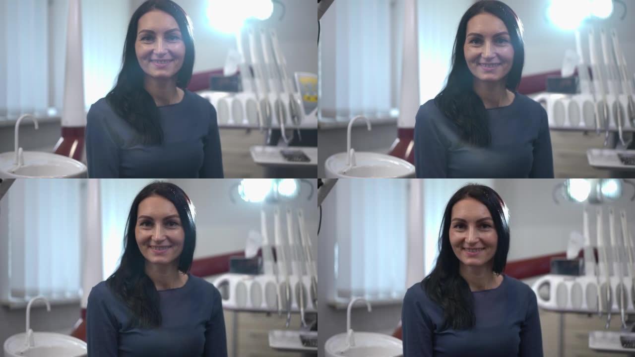 快乐的白人妇女在牙科灯光下摆姿势，背光微笑着看着相机。坐在室内诊所的满意女病人肖像。医疗保健和服务理