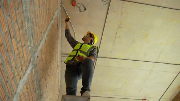 建筑工人正在爬梯子检查建筑物中的电气系统。