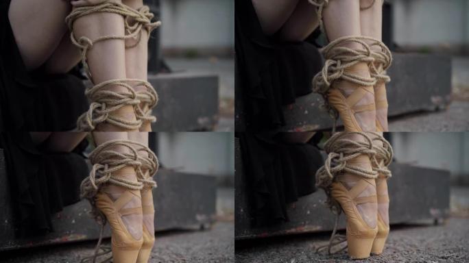 相机沿着用绳子绑住的苗条芭蕾舞女演员的腿向下移动。无法辨认的年轻白人妇女坐在户外。与职业相关的舞者概