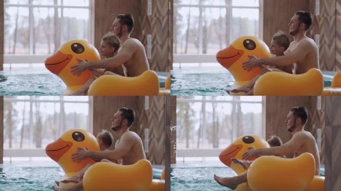 快乐的爸爸和小儿子在游泳池里骑着有趣的充气鸭，周末玩得开心，休息
