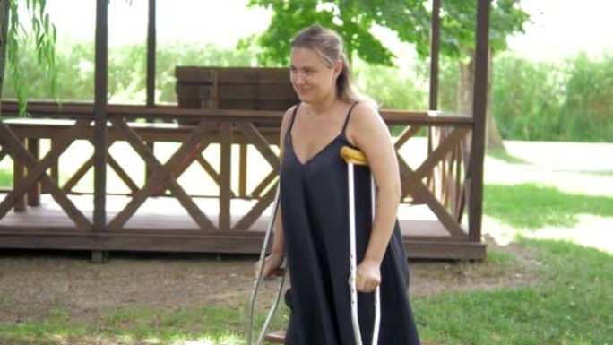 一个有石膏的年轻女孩从公园助行器上的长椅上站起来，在草地上行走。在医院外面晴朗的晴天，新鲜空气中腿部