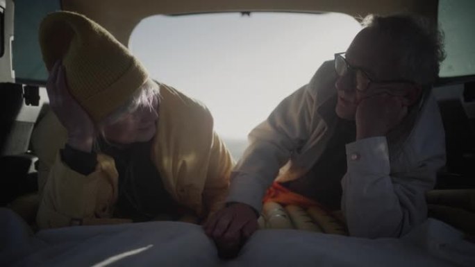 两个老年人在公路旅行中露营。躺在大型汽车后备箱里牵着手