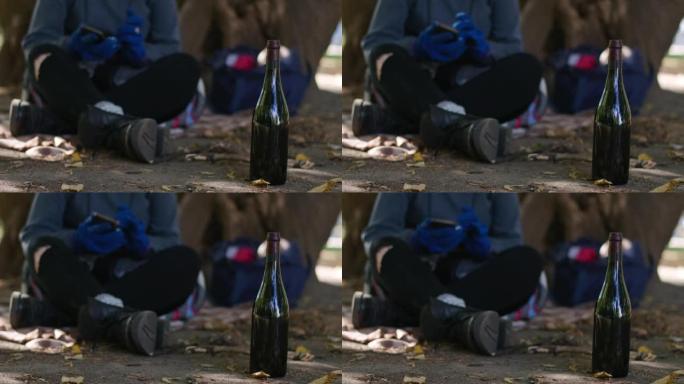 在城市公园的户外酒瓶中，无法识别的模糊无家可归的妇女在慢动作的背景下使用手机。白种人年轻酗酒成瘾者住