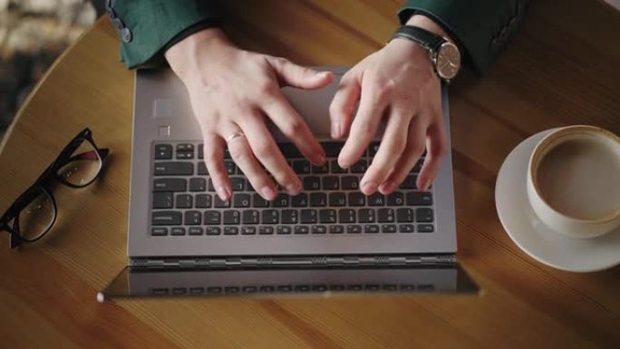 俯视图商人的手指在笔记本电脑键盘上写文字，眼镜在桌子上还有一杯咖啡在线购物和交易，经济指标