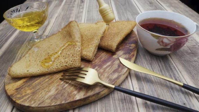 特写幻灯片。把蜂蜜倒在煎饼上。木桌上的薄煎饼茶。