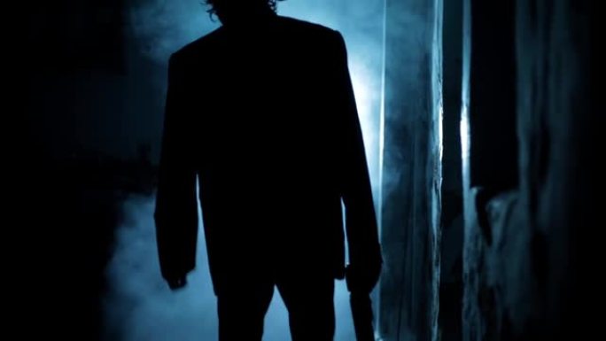 一个穿着西装的男人走在戏剧性的灯光和一些雾在他周围的电影镜头。一个男人走路的黑暗镜头。高分辨率视频。