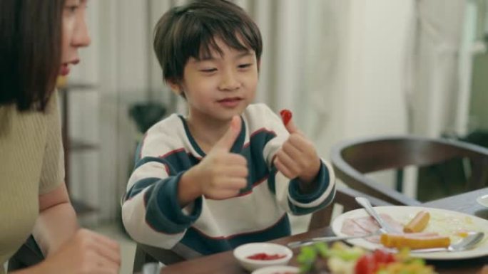 亚洲年轻的母亲和她的小男孩一起花时间在家里吃早餐。6岁的小儿子喜欢吃东西，用手指放进番茄酱碗。玩食物