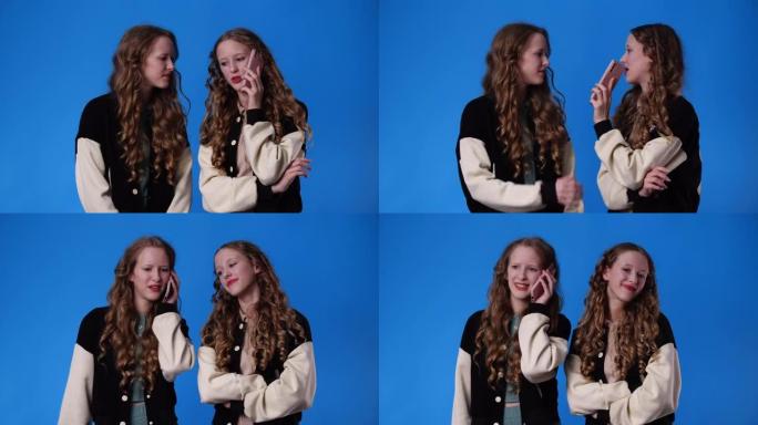 4k慢动作视频，双胞胎女孩在蓝色背景下通过电话交谈。