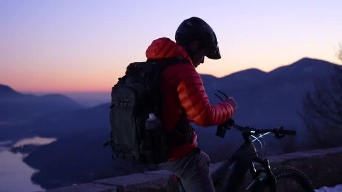 山地车手在日落之后的蓝色时刻放松，欣赏下面的湖泊和山脉