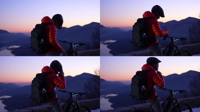 山地车手在日落之后的蓝色时刻放松，欣赏下面的湖泊和山脉