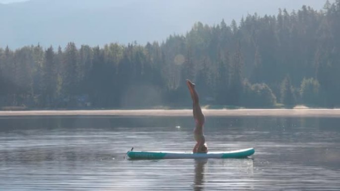 年轻女子在站立桨板 (SUP) 上执行瑜伽动作