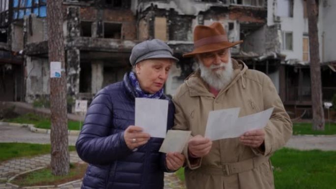 年长的悲伤的男人和女人站在照片的背景下，烧毁的住宅大楼外面。老夫妇在被炸毁的乌克兰城市回忆往事的画像