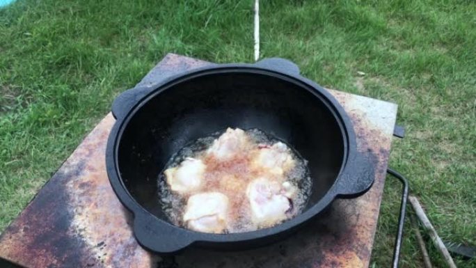 鸡大腿在沸腾的植物油中油炸。有烟和蒸汽。我们在户外用铸铁大锅做饭。特写。