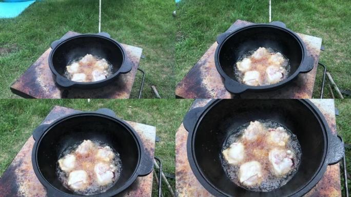 鸡大腿在沸腾的植物油中油炸。有烟和蒸汽。我们在户外用铸铁大锅做饭。特写。