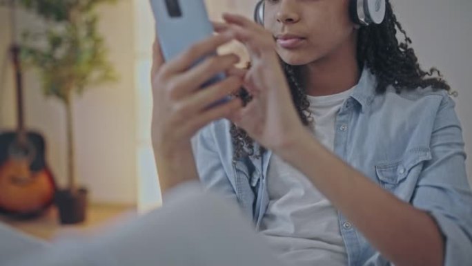 戴着耳机的黑人青少年在电话上的社交网络中聊天，小工具成瘾