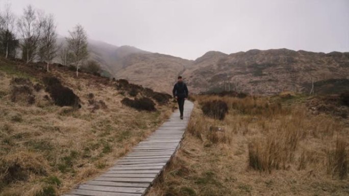 苏格兰高地开始下雨时，背着书包的人沿着木板路散步