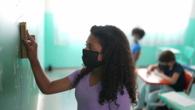 一个女孩戴着防护口罩在教室里擦黑板的肖像