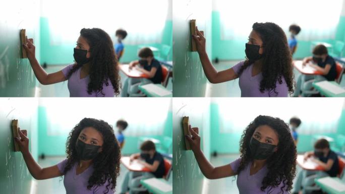一个女孩戴着防护口罩在教室里擦黑板的肖像