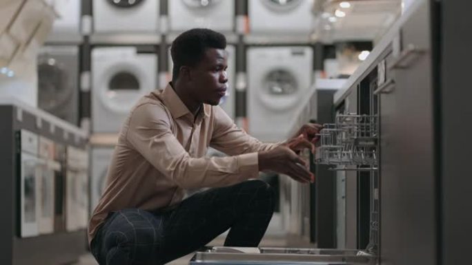 美国黑人成人正在家电商店中选择洗碗机，打开门并检查内部