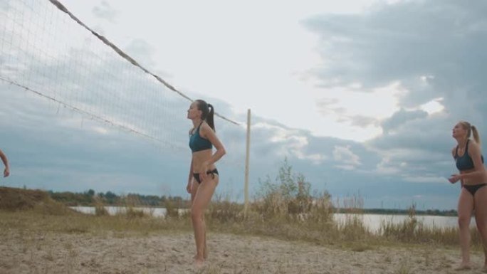活跃的年轻女性在夏季多云的天气里打沙滩排球，在桑迪球场上跳跃和奔跑，健康的生活方式