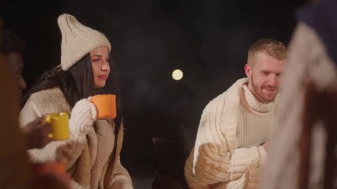 快乐的年轻人围坐在篝火旁，讲有趣的故事，在冬夜喝热茶