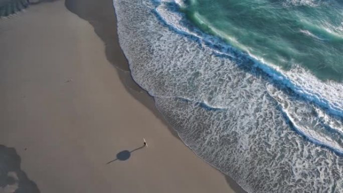 英国南部沿海海滩的空中无人机视图，冲浪者沿着海滩散步